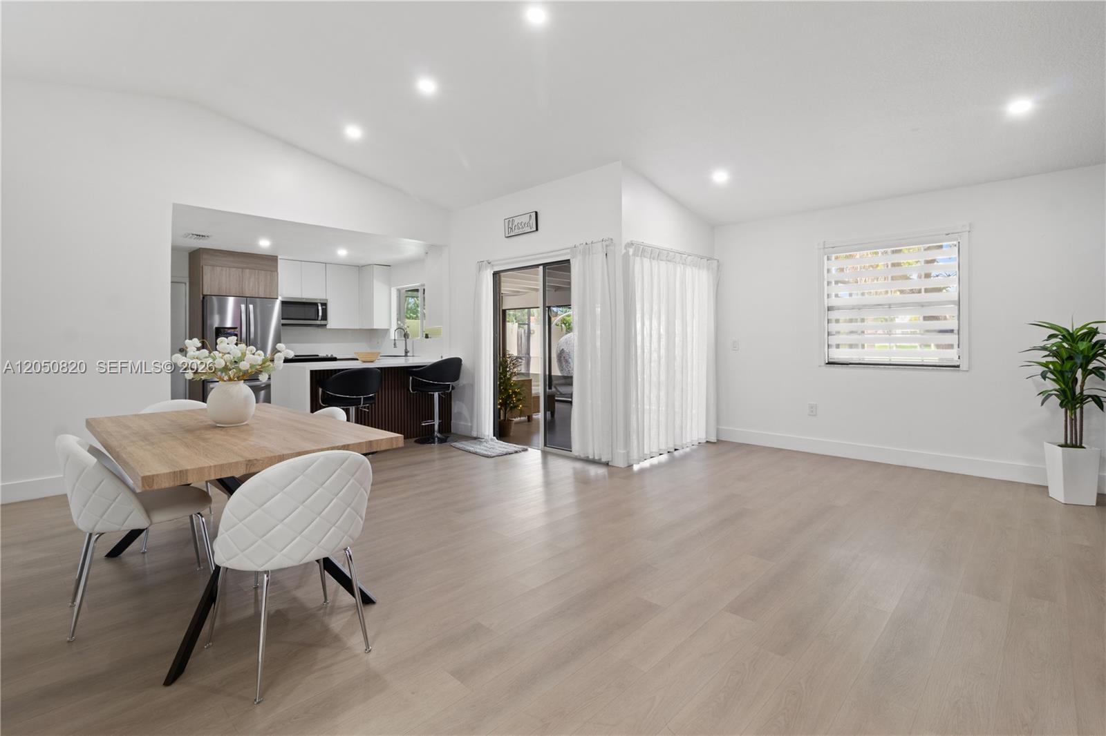 A dining area with light wood flooring opens into a kitchen with a breakfast bar — 10626 SW 148th Ave Dr, Miami FL 33196, MIAMI, FL