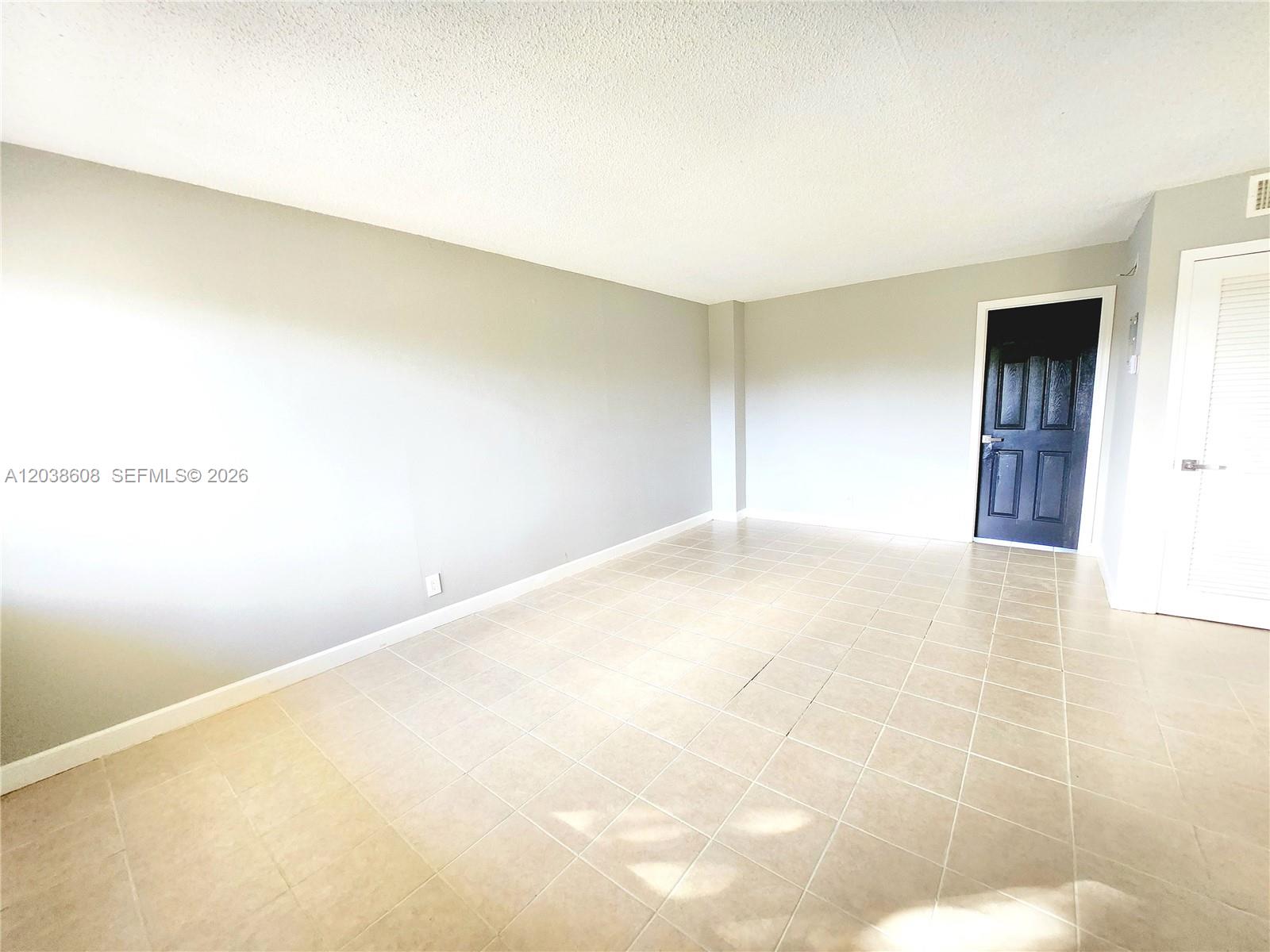 An empty room features light gray walls, beige tile flooring, and a dark entry door — 191 SW 15th St # 202, Pompano Beach FL 33060, POMPANO BEACH, FL