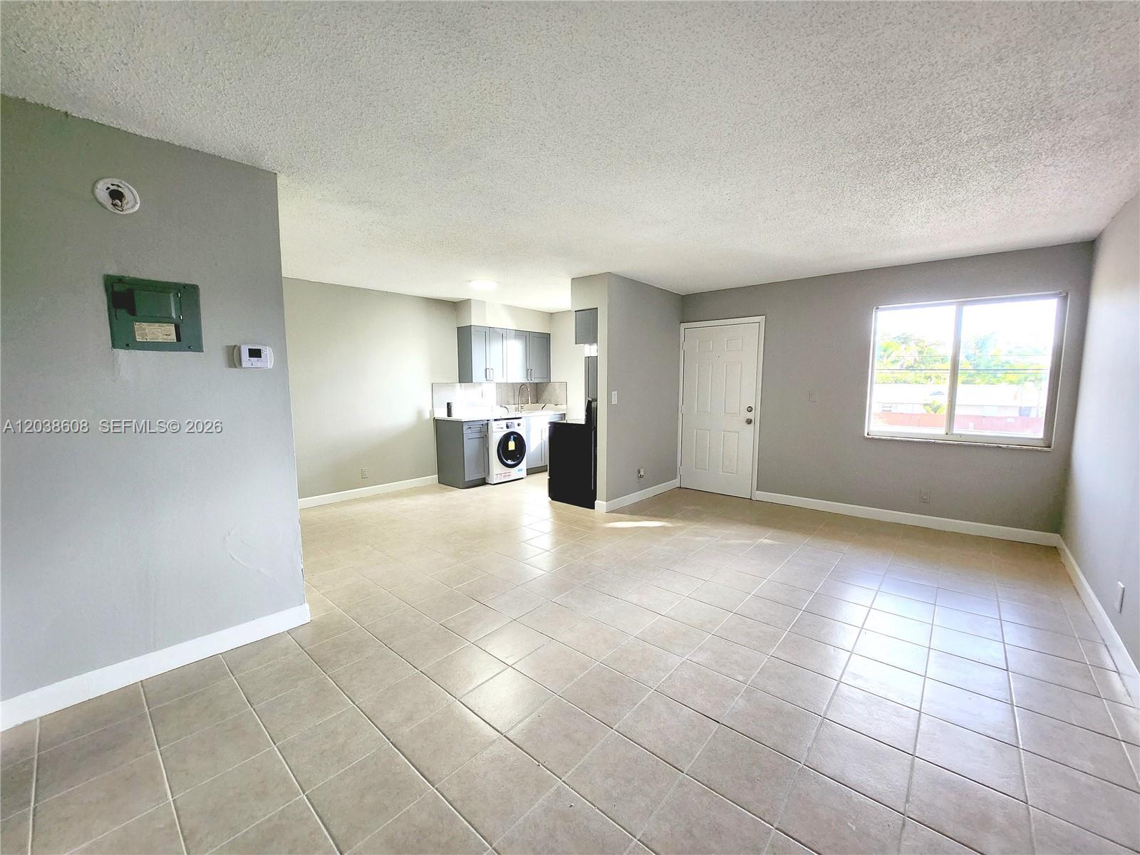 An open-concept living area features tiled floors, a small kitchen with laundry, and a window — 191 SW 15th St # 202, Pompano Beach FL 33060, POMPANO BEACH, FL