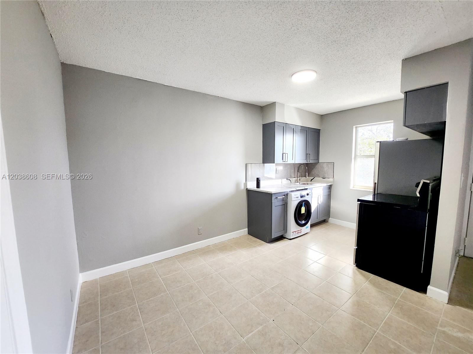 A kitchen features gray cabinets, a white washing machine, and black appliances on tiled flooring — 191 SW 15th St # 202, Pompano Beach FL 33060, POMPANO BEACH, FL