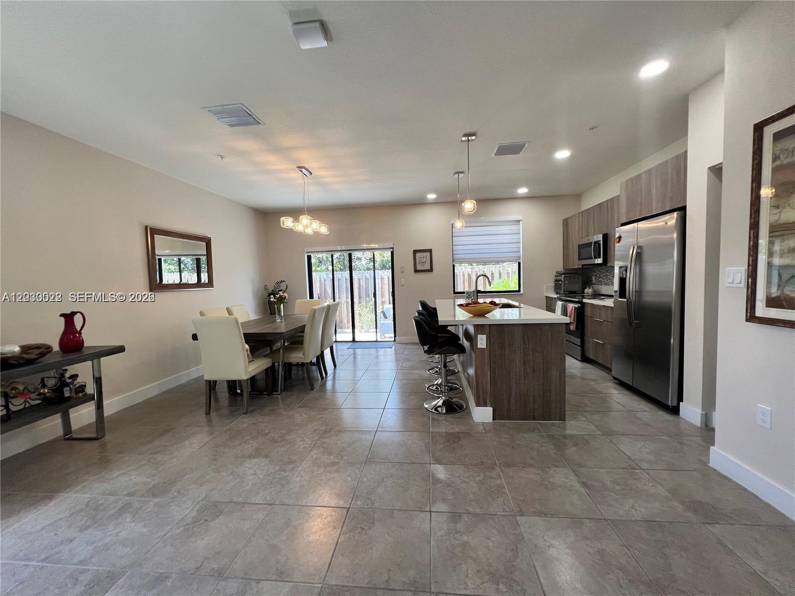 An open-concept kitchen and dining area features tile flooring, stainless steel appliances, and a breakfast bar — 10455 NW 82nd St # 1, Doral FL 33178, DORAL, FL