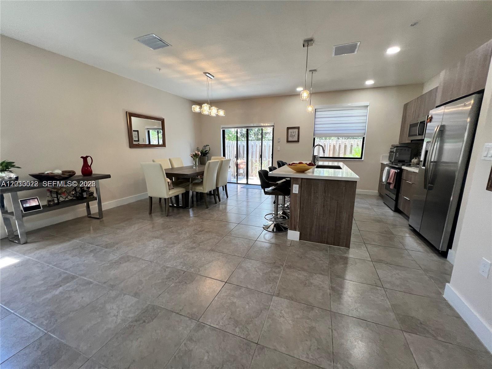 An open-concept kitchen and dining area features tile flooring, stainless steel appliances, and pendant lighting — 10455 NW 82nd St # 1, Doral FL 33178, DORAL, FL