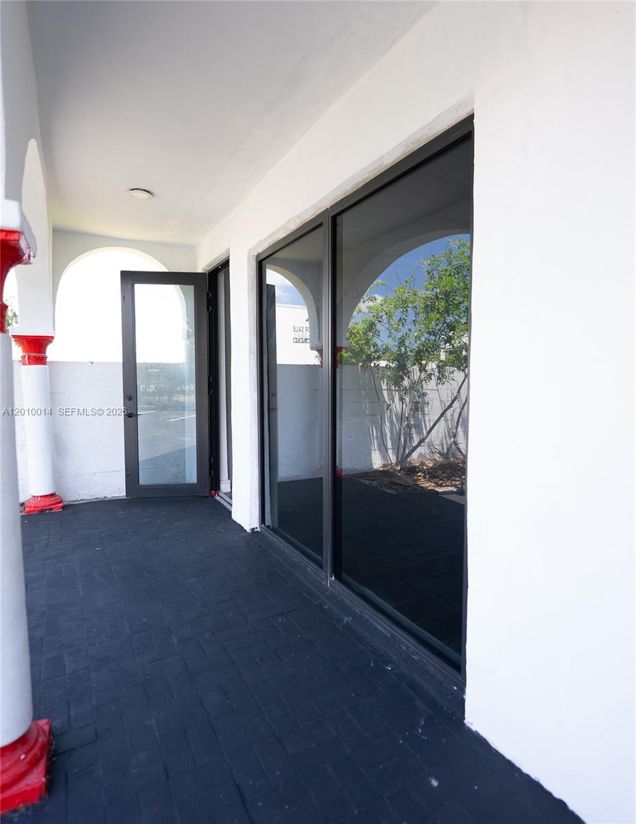 A covered patio features black brick flooring, white walls, and a glass door entrance — 88 NW 54th St, Miami FL 33127, MIAMI, FL