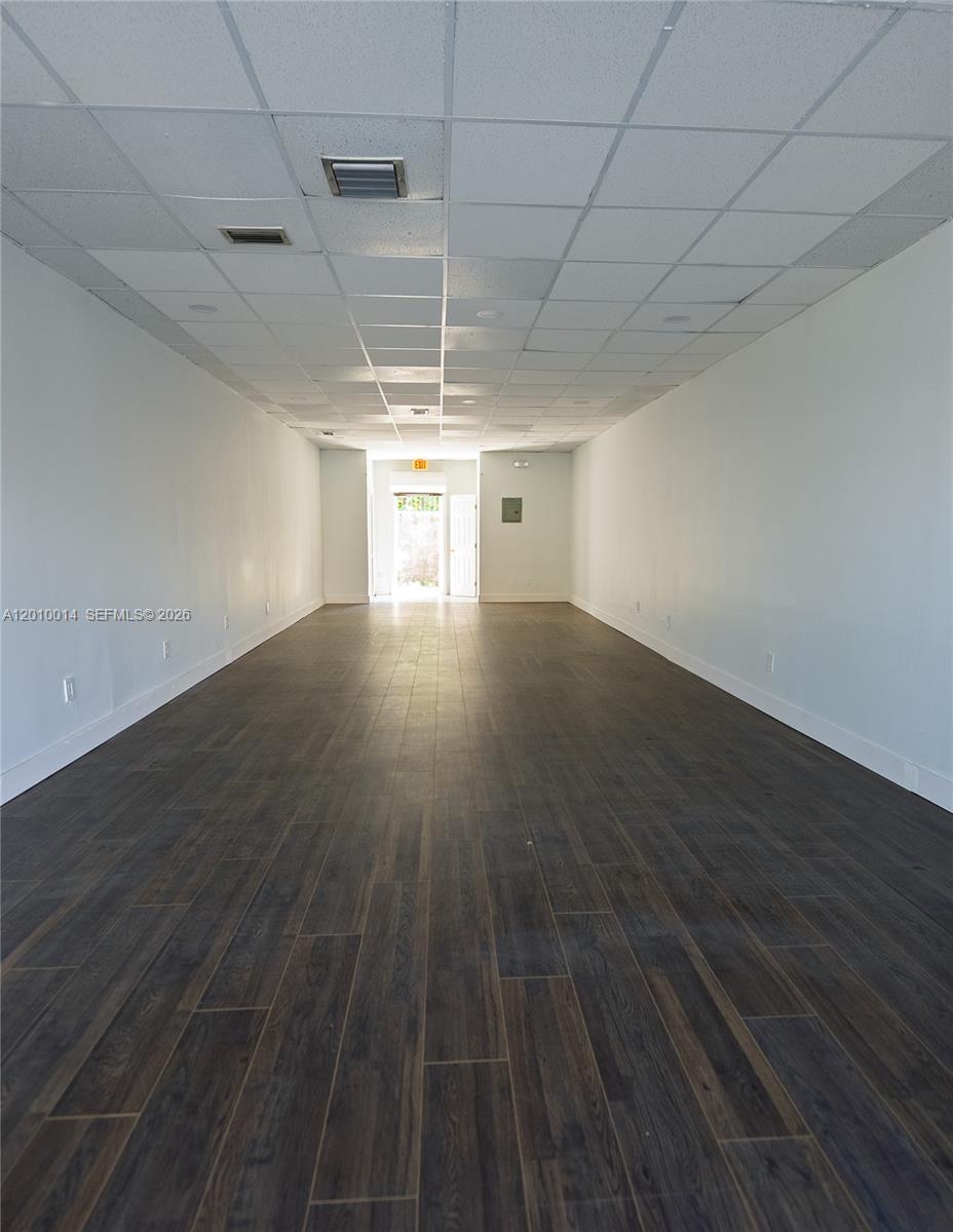 A long, empty commercial space features white walls, a drop ceiling, and dark wood-look flooring — 88 NW 54th St, Miami FL 33127, MIAMI, FL