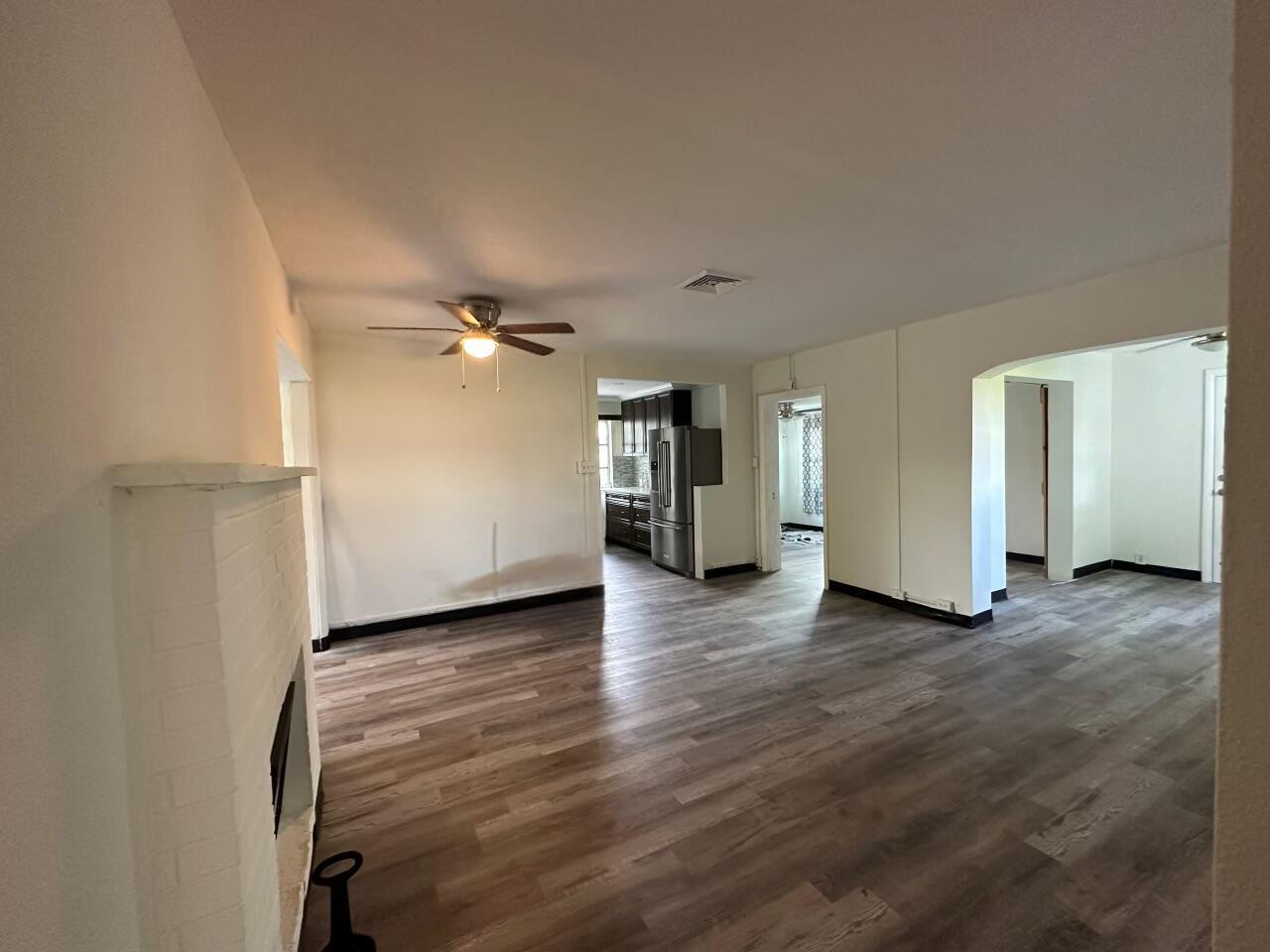 An open living area with wood-look flooring, a white brick fireplace, and a ceiling fan — 84 E North Shore Avenue, FL 33917, FL