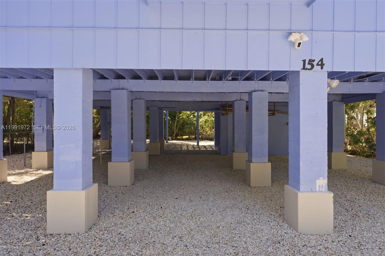 The underside of an elevated house features multiple blue support pillars on a gravel ground — 154 Sebring Dr, Tavernier FL 33070, TAVERNIER, FL