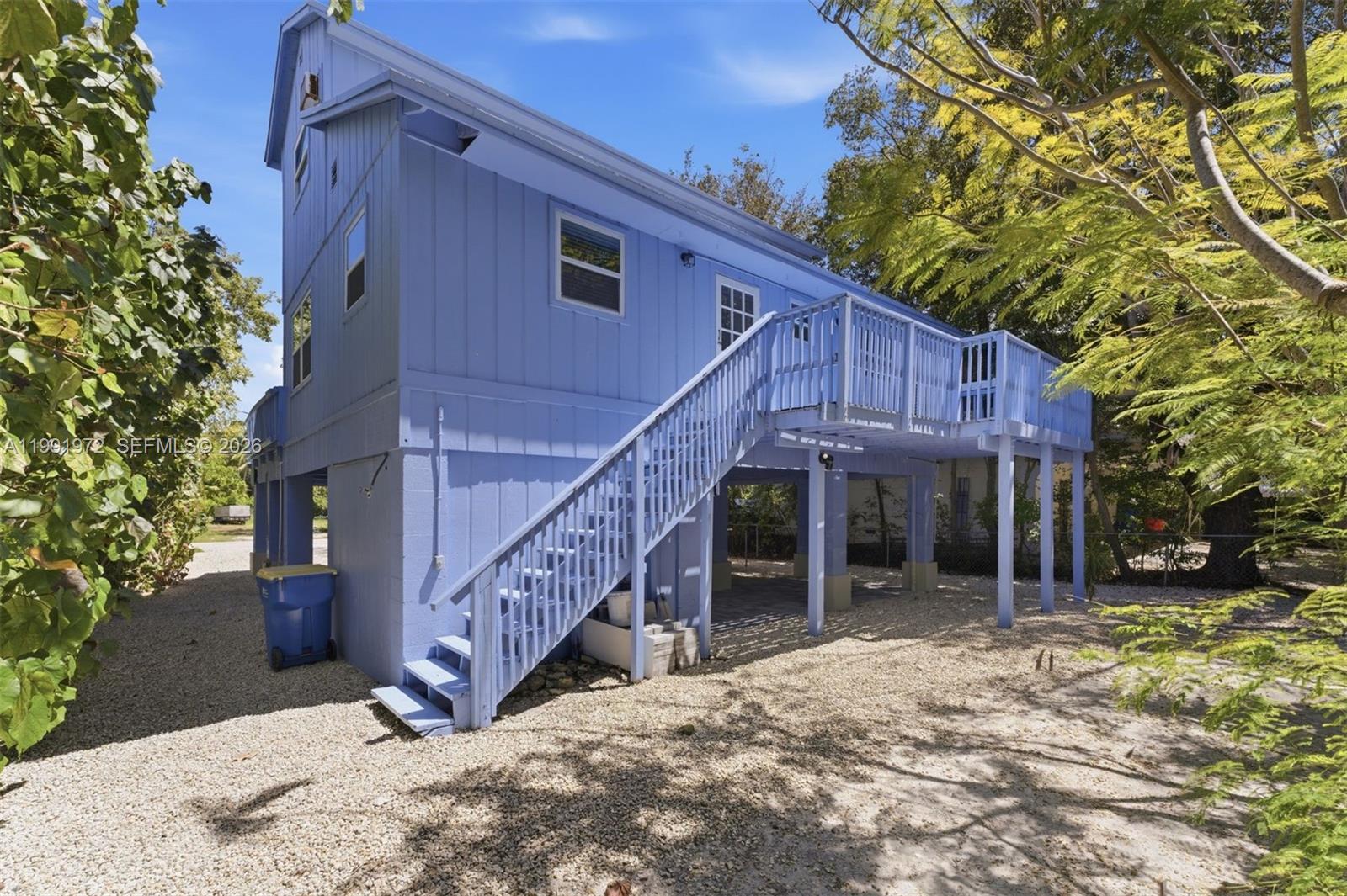 A light blue elevated house features a wooden staircase leading to a second-story deck — 154 Sebring Dr, Tavernier FL 33070, TAVERNIER, FL