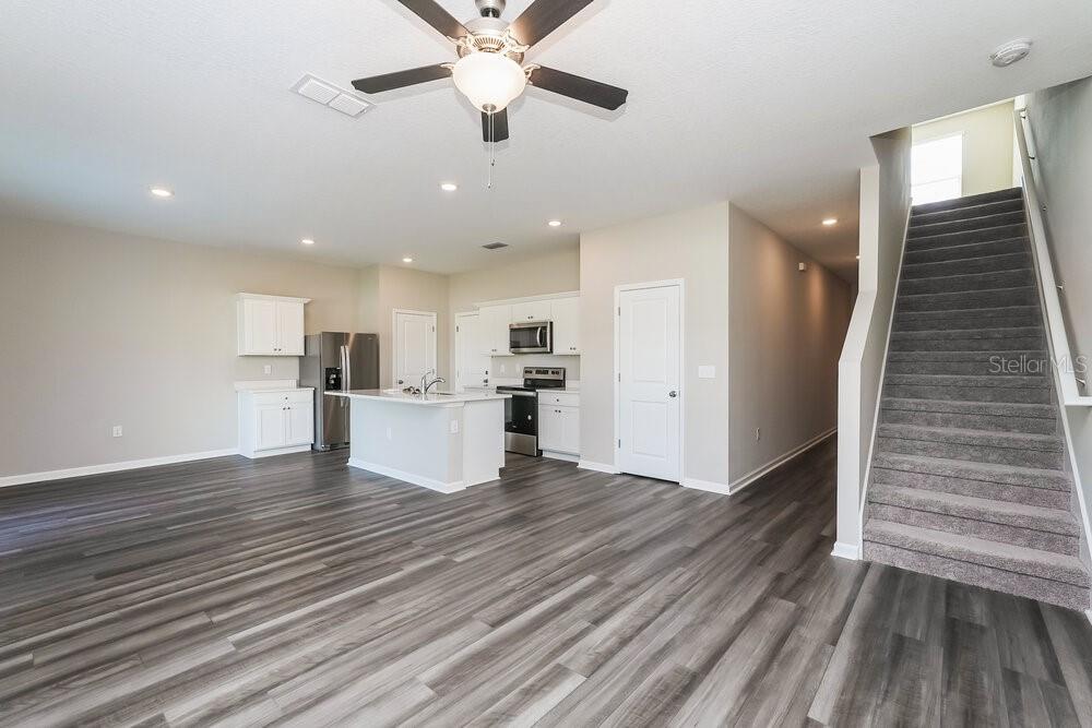 An open-concept kitchen and living area with gray wood-look flooring and a carpeted staircase — 962 KELLY FERN LOOP, RUSKIN, FL