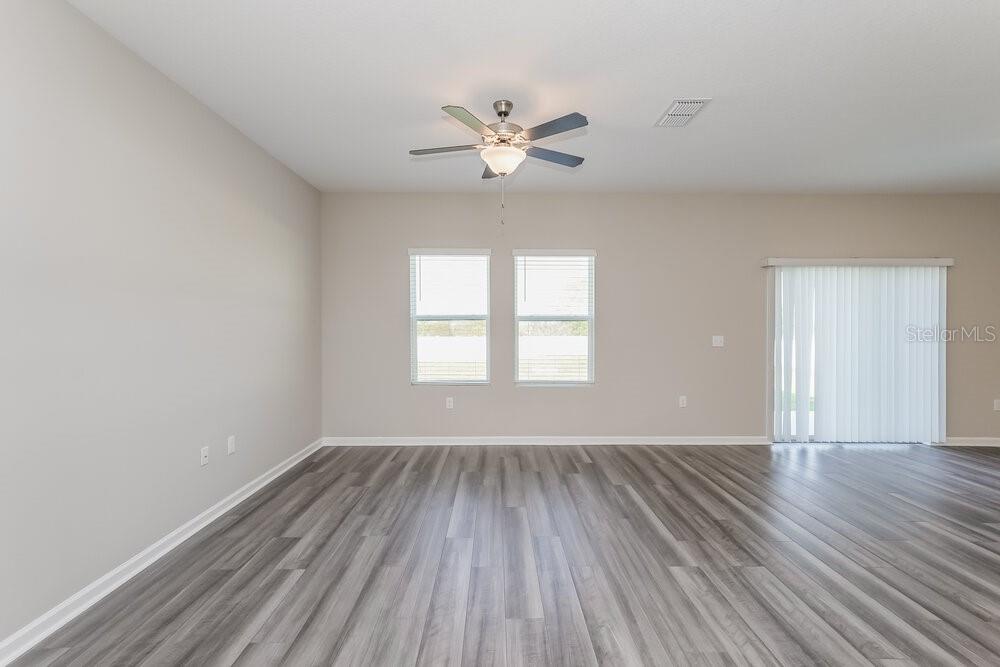 An empty living room features light gray walls, wood-look flooring, a ceiling fan, and windows — 962 KELLY FERN LOOP, RUSKIN, FL