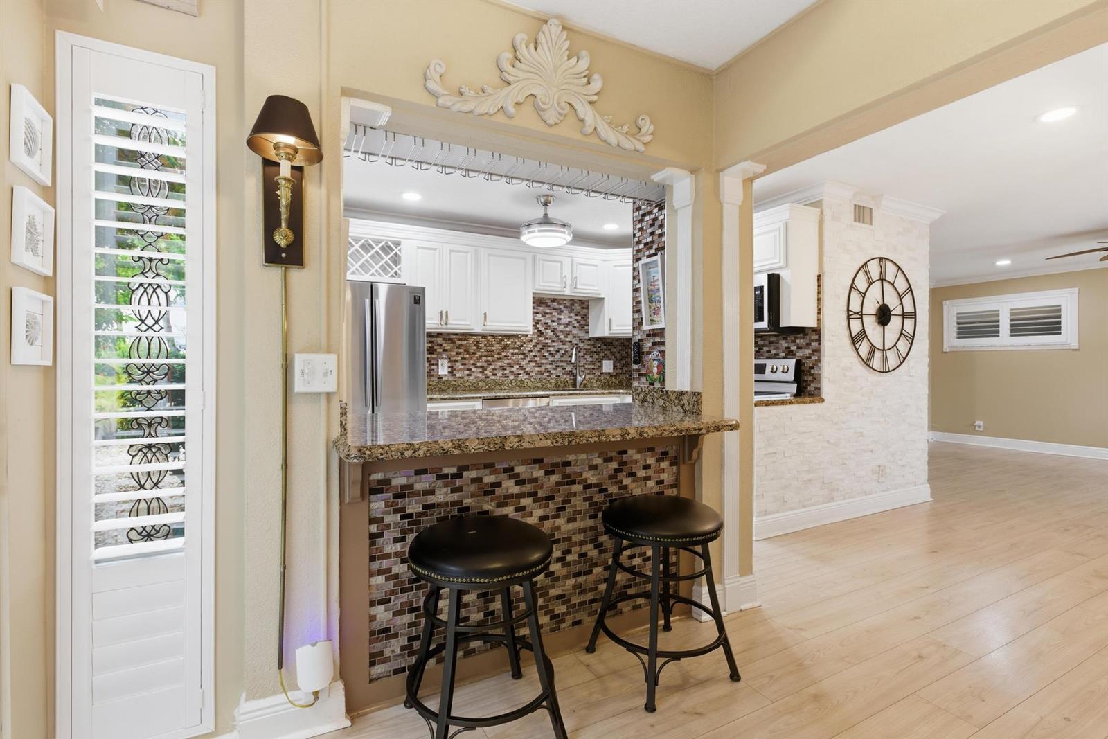 A kitchen pass-through features a granite breakfast bar, mosaic tile, and two bar stools — 34 Colonial Club Drive # 101, Boynton Beach FL 33435, BOYNTON BEACH, FL