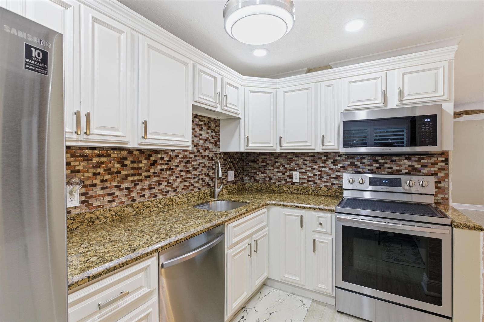 A kitchen features white cabinets, granite countertops, a mosaic tile backsplash, and stainless steel appliances — 34 Colonial Club Drive # 101, Boynton Beach FL 33435, BOYNTON BEACH, FL