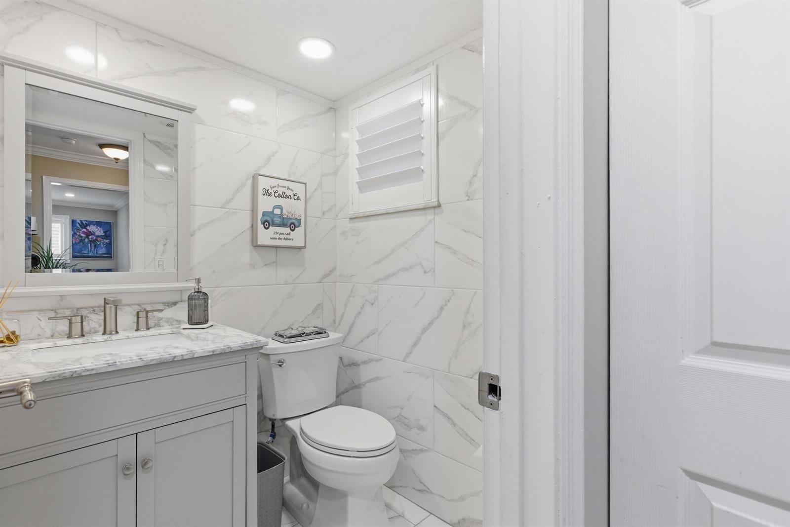A bathroom features a gray vanity with a marble countertop, white marble-look wall tiles, and toilet — 34 Colonial Club Drive # 101, Boynton Beach FL 33435, BOYNTON BEACH, FL