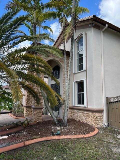 A two-story house exterior features a stone-accented entrance, palm trees, and tall vertical windows — 1331 SW 153rd Path, Miami FL 33194, MIAMI, FL