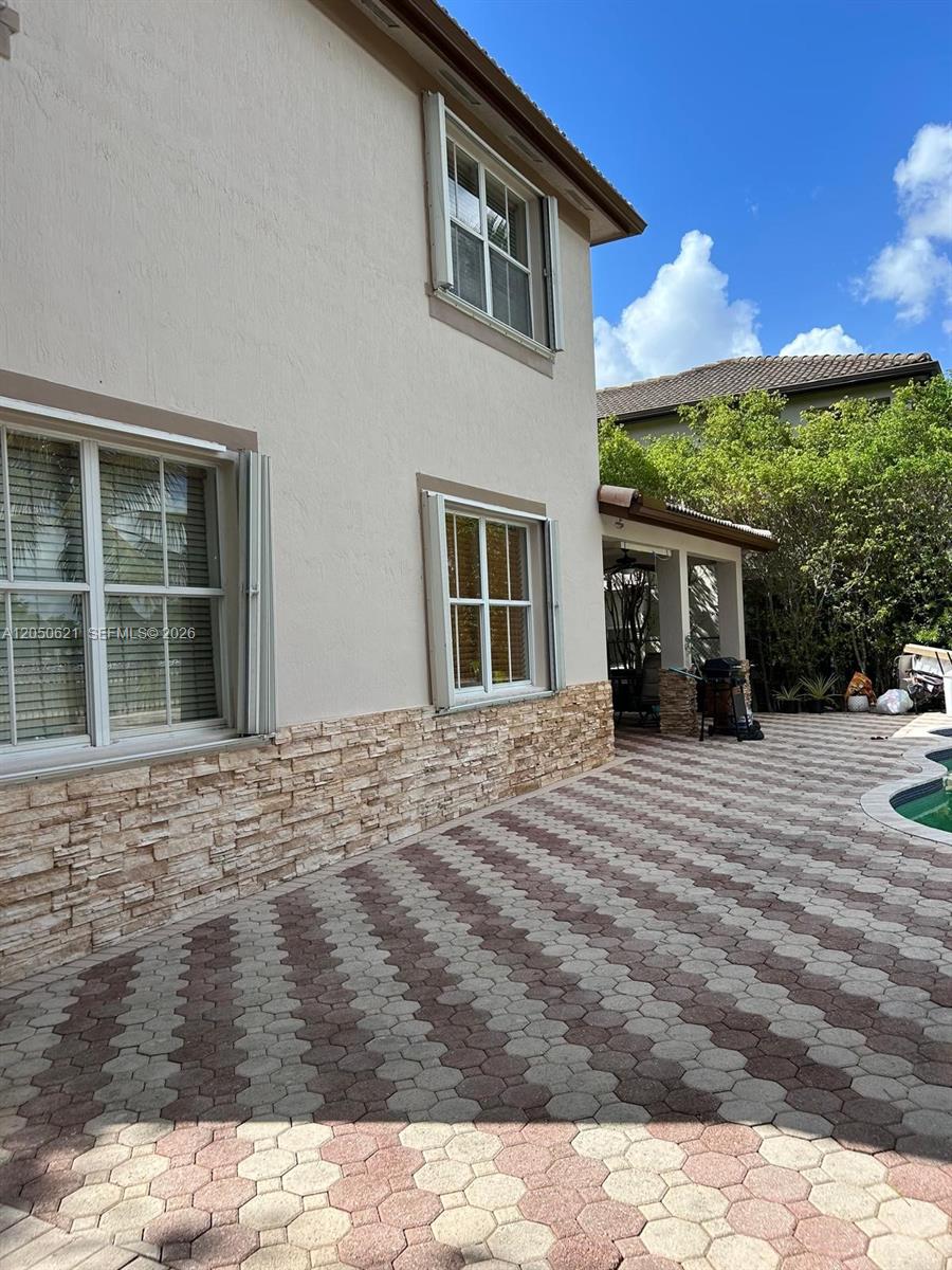 A two-story house exterior features stone veneer, white-framed windows, and a patterned paver patio — 1331 SW 153rd Path, Miami FL 33194, MIAMI, FL