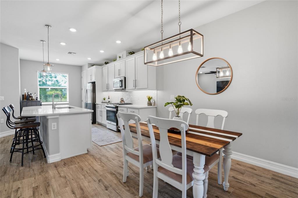 A modern kitchen features white cabinetry, a center island with bar stools, and a dining area — 4540 ALMADA LANE, WESLEY CHAPEL, FL