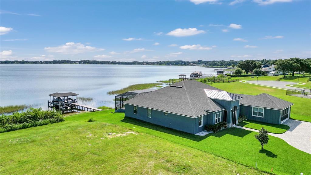 An aerial view shows a blue house with a gray roof beside a large lake — 1153 ENCLAVE COURT, AUBURNDALE, FL