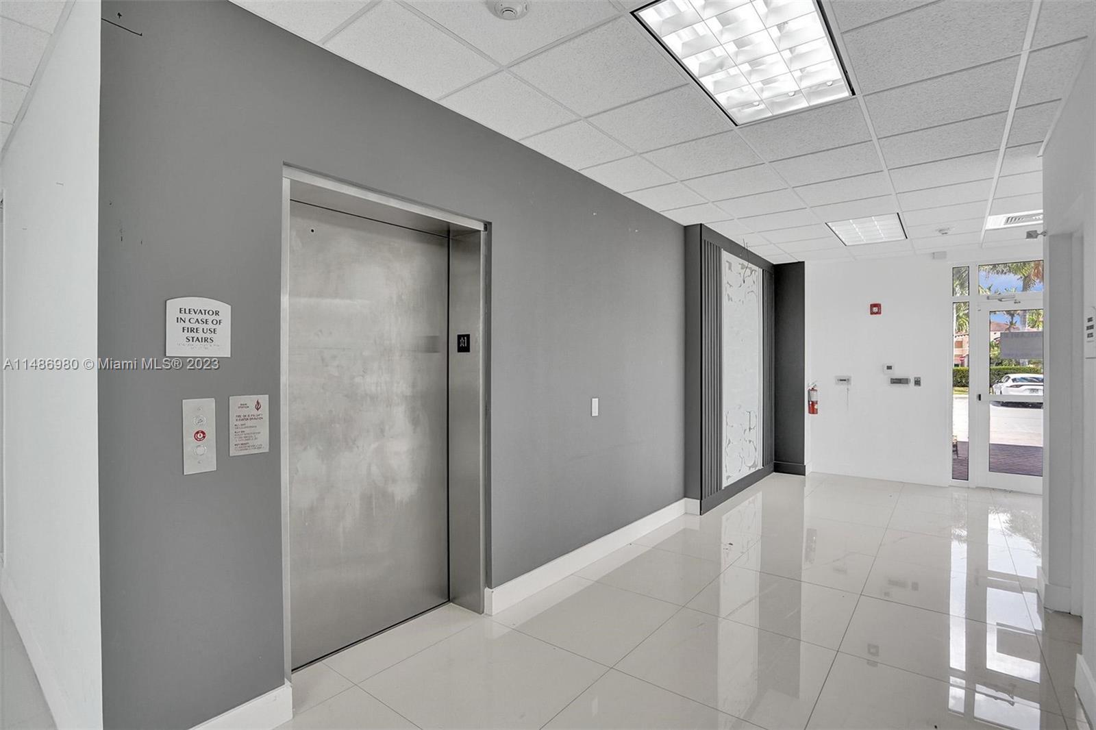 A commercial building lobby features a metal elevator, gray accent wall, and white tile flooring — 15620 SW 29th St, Miramar FL 33027, MIRAMAR, FL