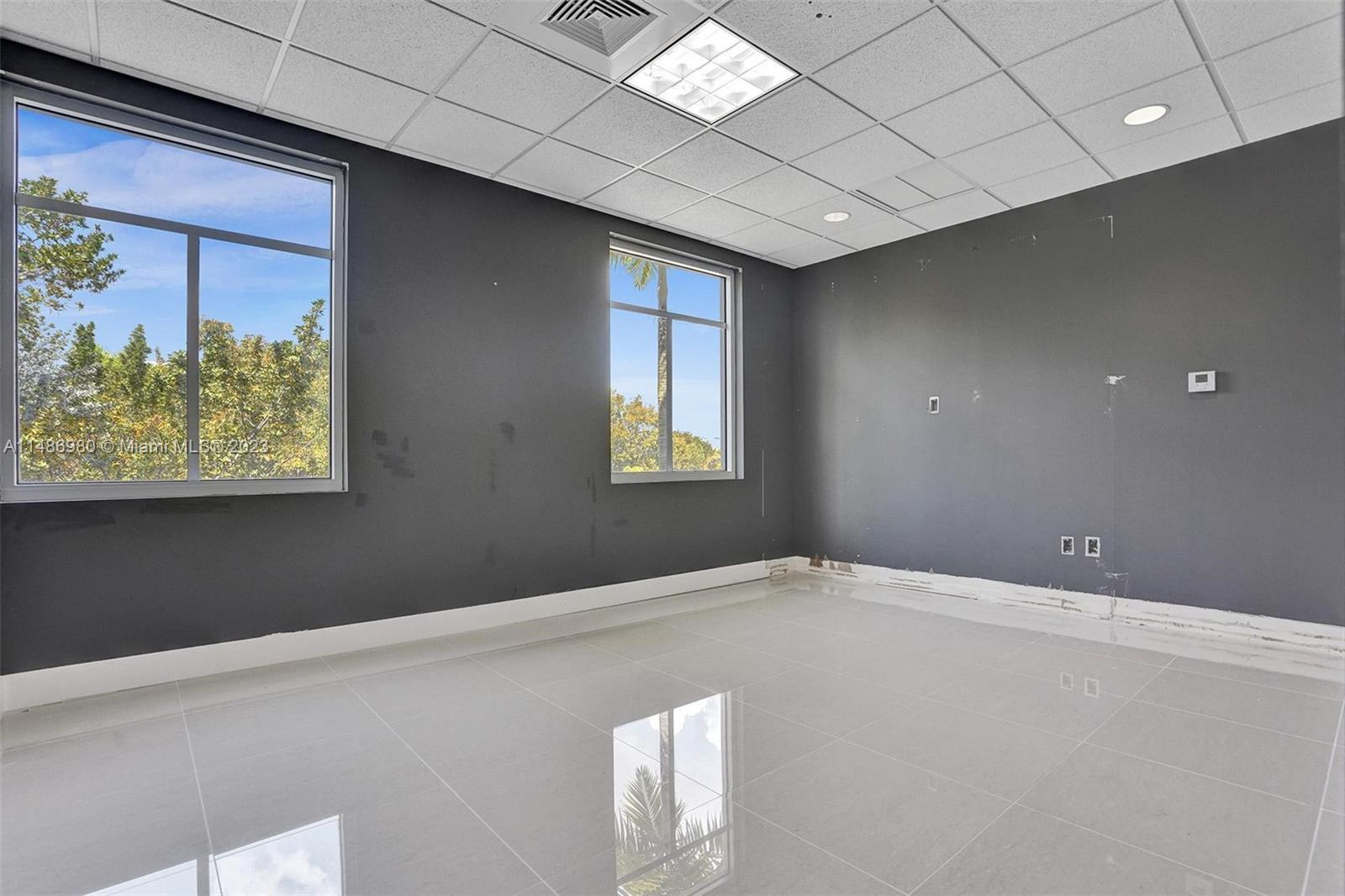 An empty office room features dark gray walls, white tile flooring, and two large windows — 15620 SW 29th St, Miramar FL 33027, MIRAMAR, FL