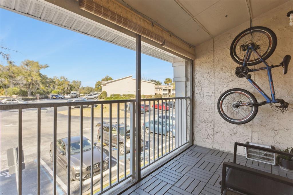 A screened-in balcony features gray interlocking floor tiles, a wall-mounted bicycle, and a parking lot view — 145 N PEARL LAKE CSWY UNIT 208, ALTAMONTE SPRINGS, FL