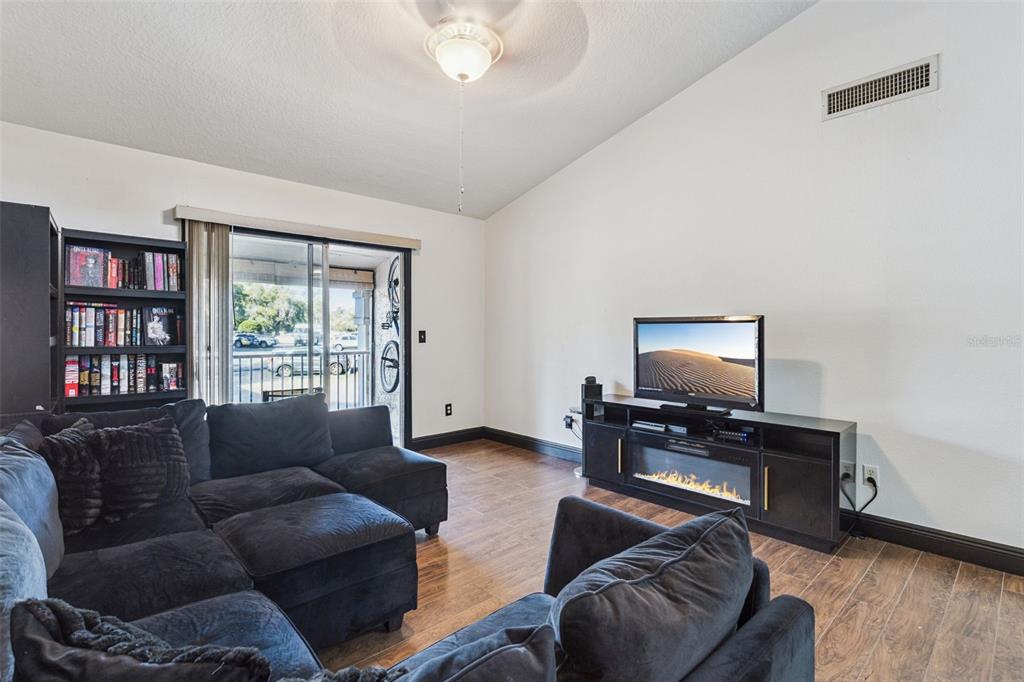 A living room features dark furniture, a fireplace media console, and a sliding glass door — 145 N PEARL LAKE CSWY UNIT 208, ALTAMONTE SPRINGS, FL
