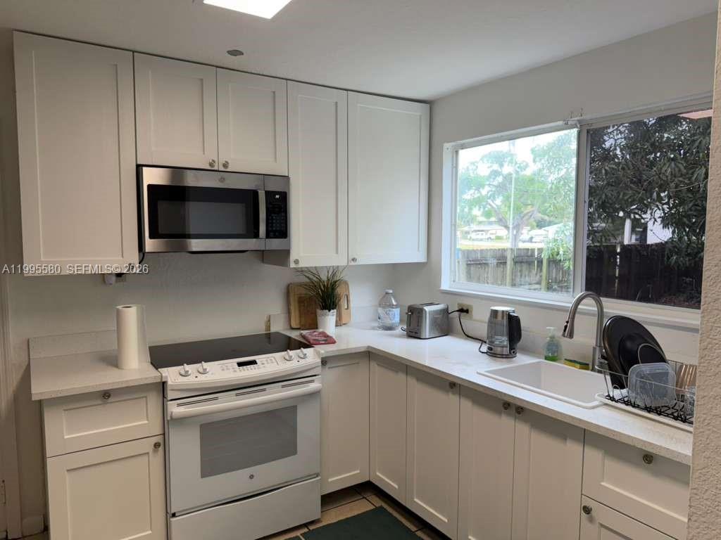 A kitchen features white cabinets, a stainless steel microwave, a white stove, and a window — 3 SW 7th Ave, Dania Beach FL 33004, DANIA BEACH, FL