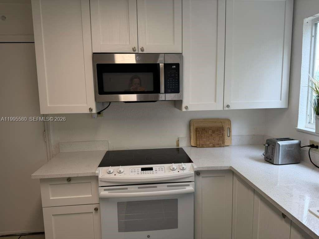 A kitchen features white cabinets, a stainless steel microwave, and a white electric range — 3 SW 7th Ave, Dania Beach FL 33004, DANIA BEACH, FL