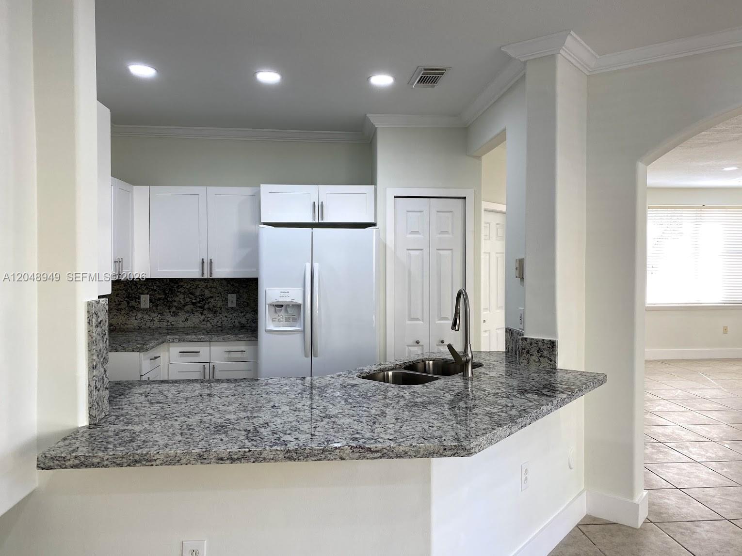 A kitchen features white cabinetry, granite countertops, and a stainless steel sink on a peninsula — 4874 NW 107th Path, Doral FL 33178, DORAL, FL