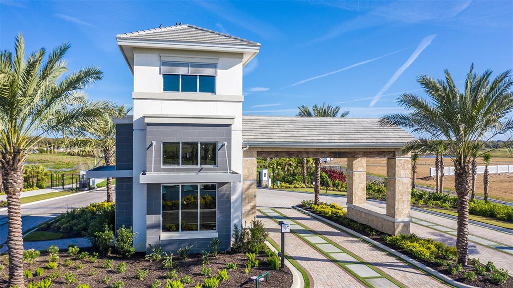An exterior view of a gated community entrance with a stone guardhouse and palm trees — 7824 CENTAURUS WAY, SARASOTA, FL