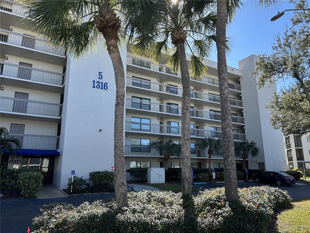 A multi-story apartment building features balconies, palm trees, and a parking lot in front — 1316 PASADENA AVENUE S UNIT 202, SOUTH PASADENA, FL