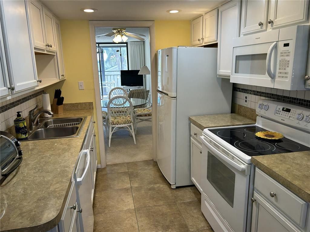 A galley kitchen features white cabinets, tan countertops, and a view into a dining area — 1316 PASADENA AVENUE S UNIT 202, SOUTH PASADENA, FL