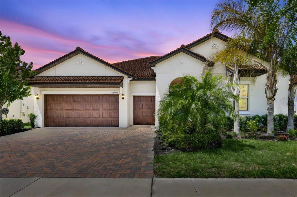 A single-story house with a two-car garage, a paver driveway, and palm trees at sunset — 16955 SCUBA CREST STREET, WIMAUMA, FL