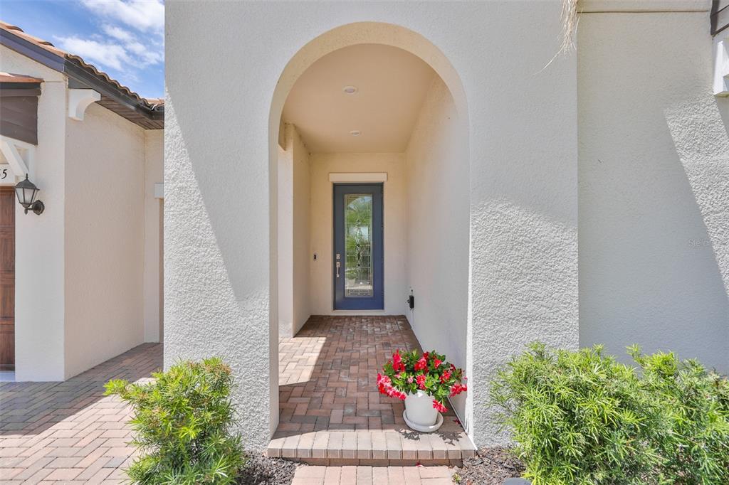 A blue front door is set within an arched entryway featuring brick flooring and stucco walls — 16955 SCUBA CREST STREET, WIMAUMA, FL
