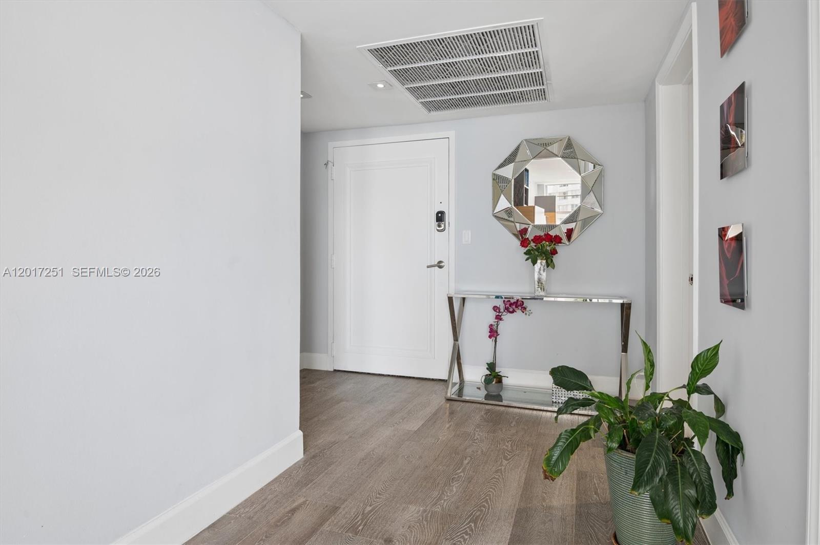 A modern entryway features wood-look flooring, a console table, a geometric mirror, and a plant — 5660 Collins Ave # 6C, Miami Beach FL 33140, MIAMI BEACH, FL