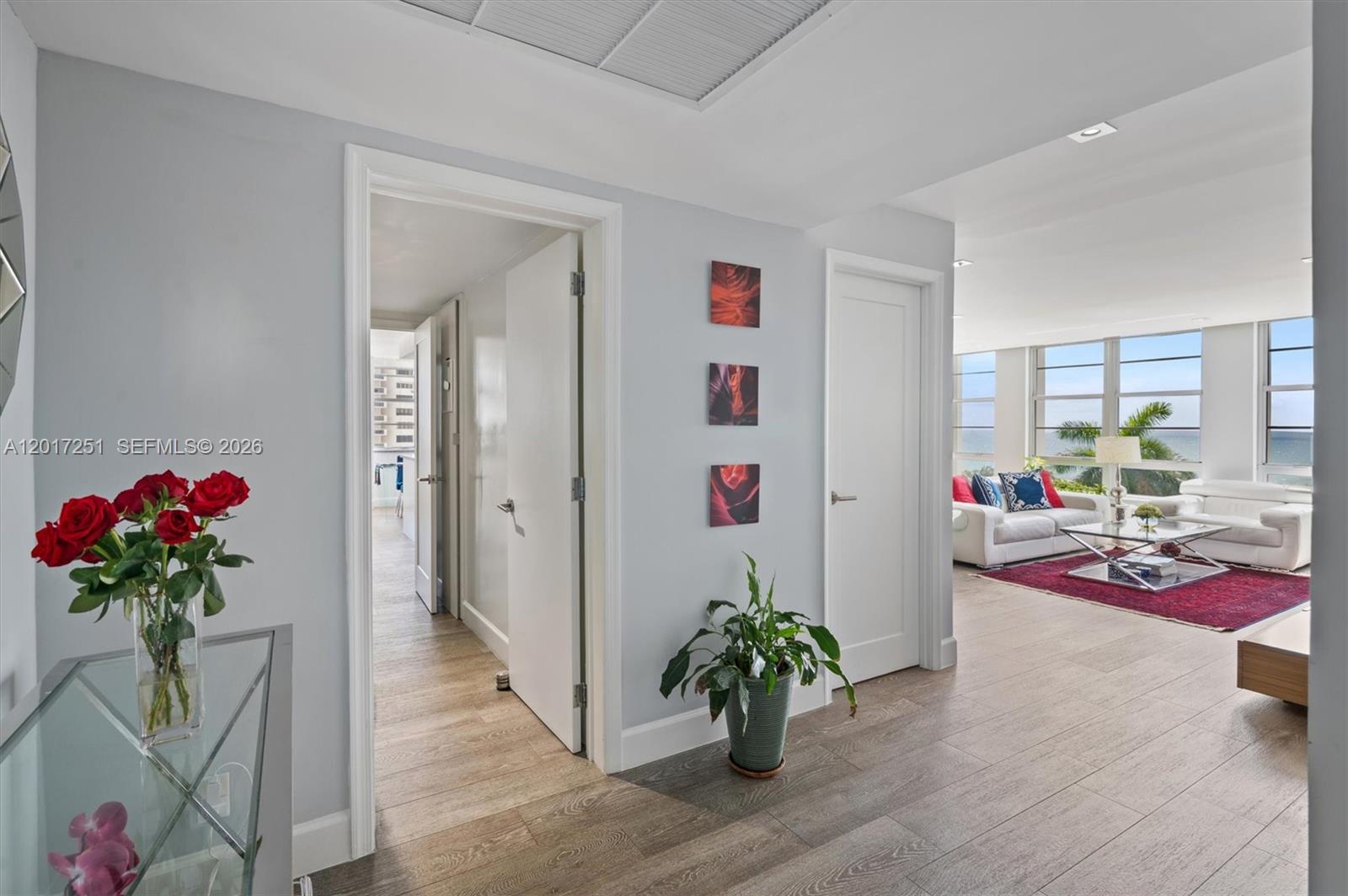 A hallway with light wood floors leads to a living room with ocean views — 5660 Collins Ave # 6C, Miami Beach FL 33140, MIAMI BEACH, FL