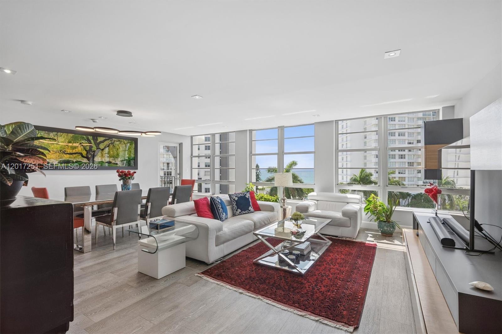 A bright living and dining area features white furniture, a red rug, and ocean views — 5660 Collins Ave # 6C, Miami Beach FL 33140, MIAMI BEACH, FL