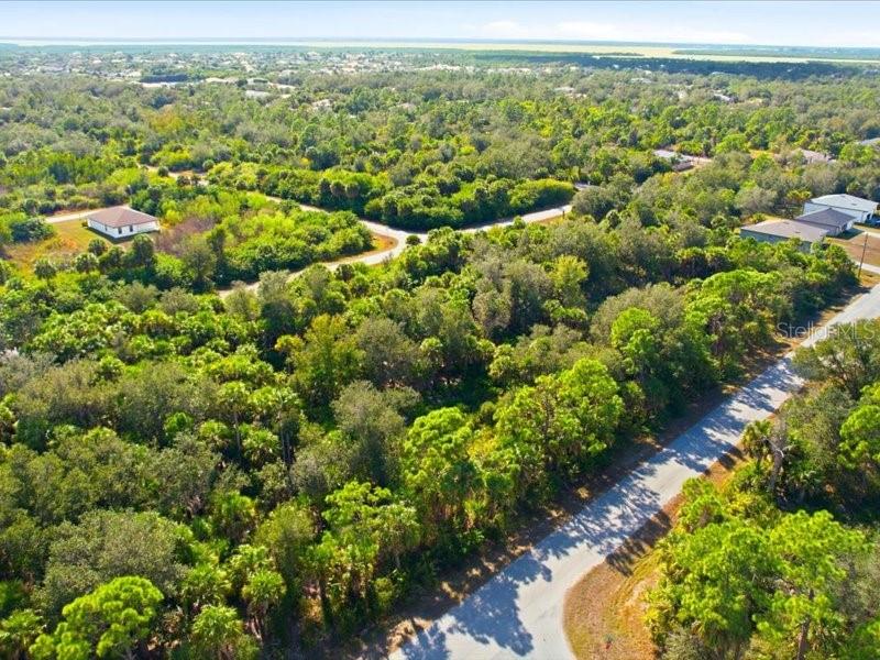 An aerial view shows a paved road winding through a wooded area with scattered houses — 17378 QUINCY AVENUE, PORT CHARLOTTE, FL