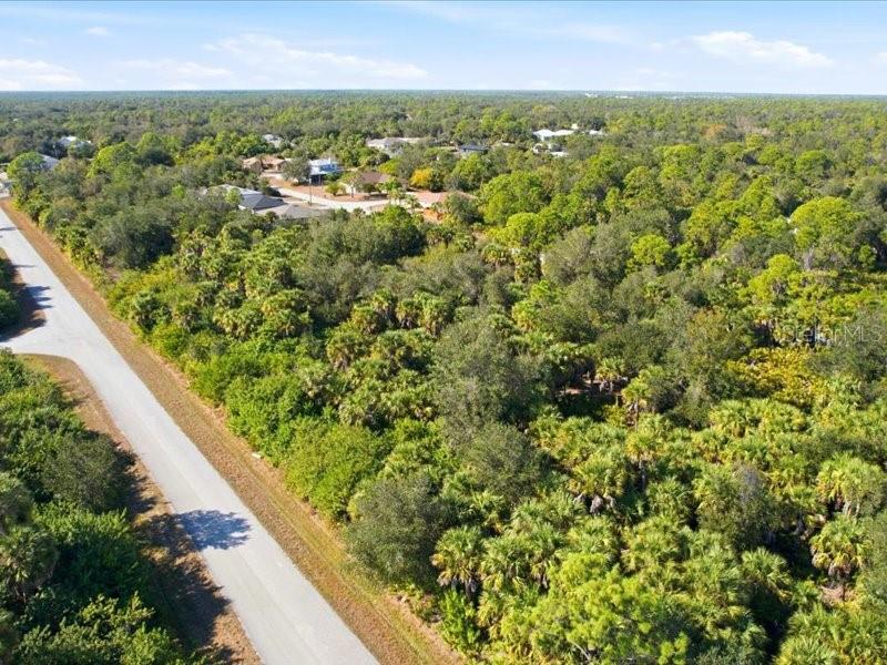 An aerial view shows a paved road bordering a dense, wooded lot — 17378 QUINCY AVENUE, PORT CHARLOTTE, FL