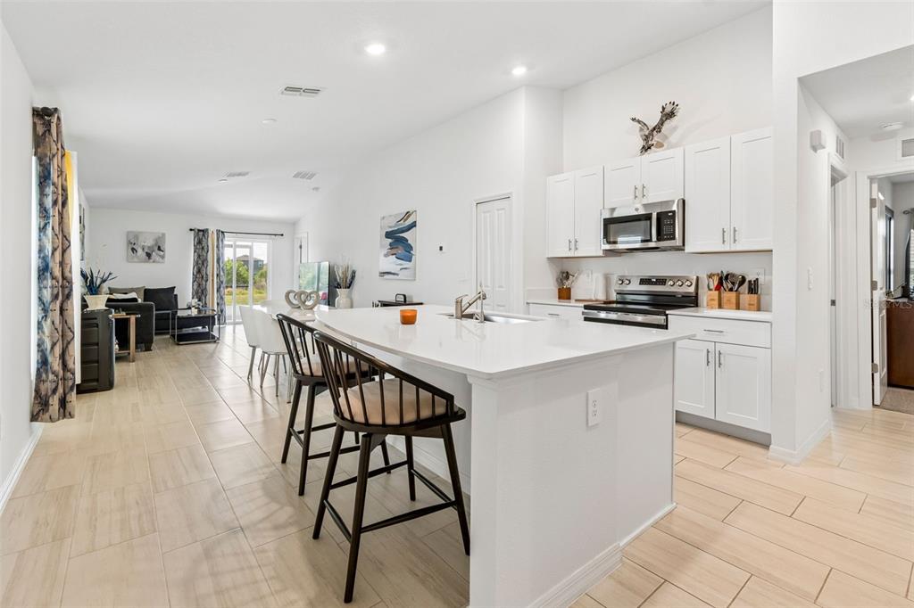 A white kitchen with an island and bar stools opens into a living area — 3511 GREAT PARK CT, PLANT CITY, FL