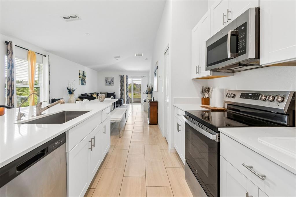 A modern kitchen with white cabinets and quartz countertops opens into a bright living area — 3511 GREAT PARK CT, PLANT CITY, FL