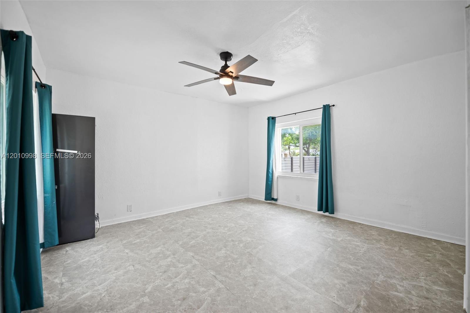 An empty bedroom features white walls, a ceiling fan, teal curtains, and tiled flooring — 1199 NW 121st St, North Miami FL 33168, NORTH MIAMI, FL