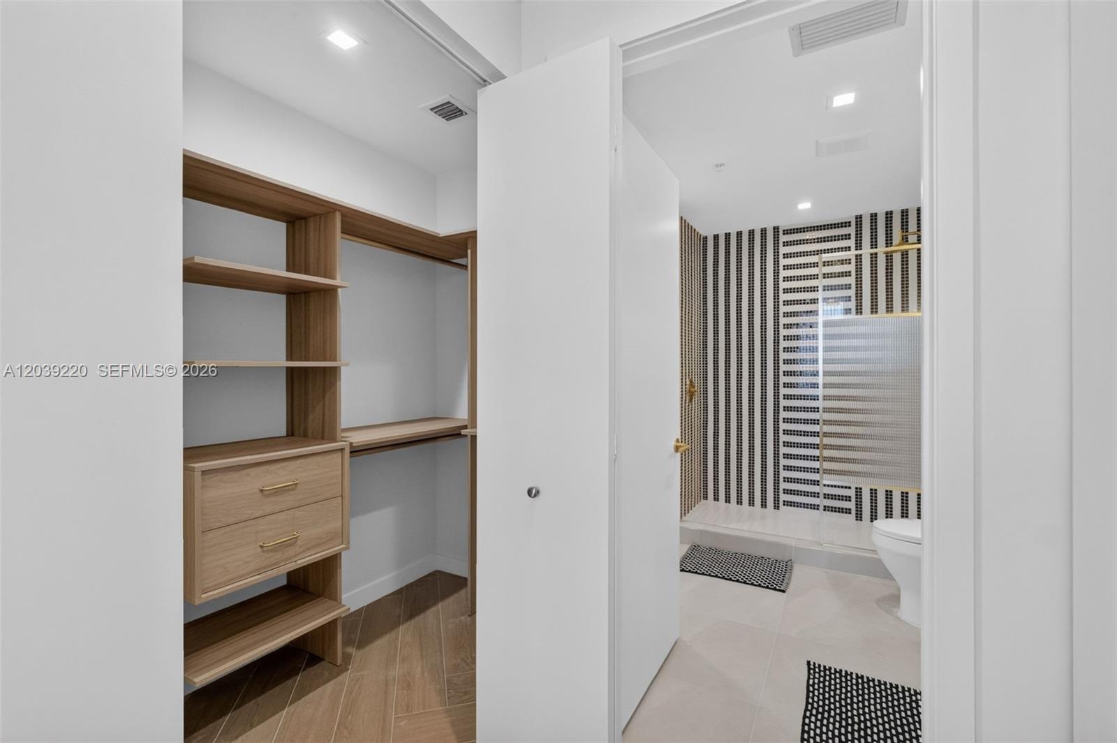 A walk-in closet with wooden shelving and drawers opens into a modern tiled bathroom — 2700 NW 2ND AVE # 528, Miami FL 33127, MIAMI, FL