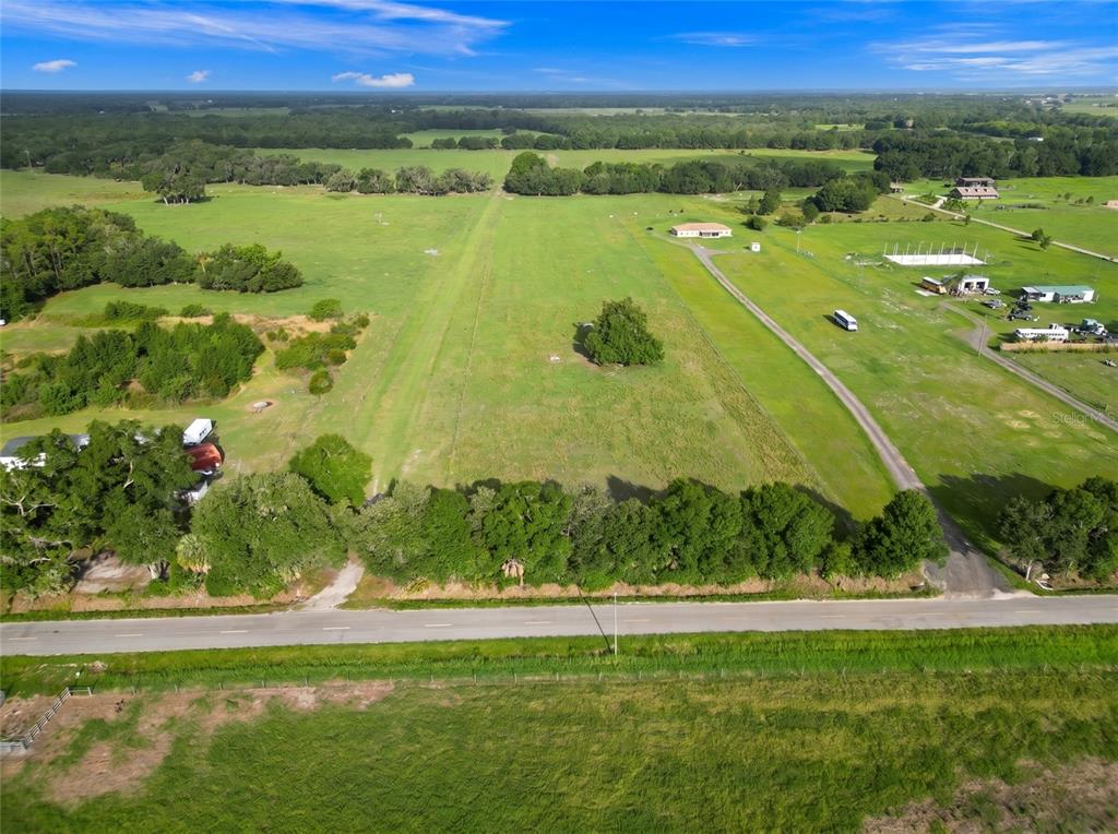 An aerial view shows a large, grassy field with a driveway and scattered trees — N ED WELLS ROAD, WAUCHULA, FL