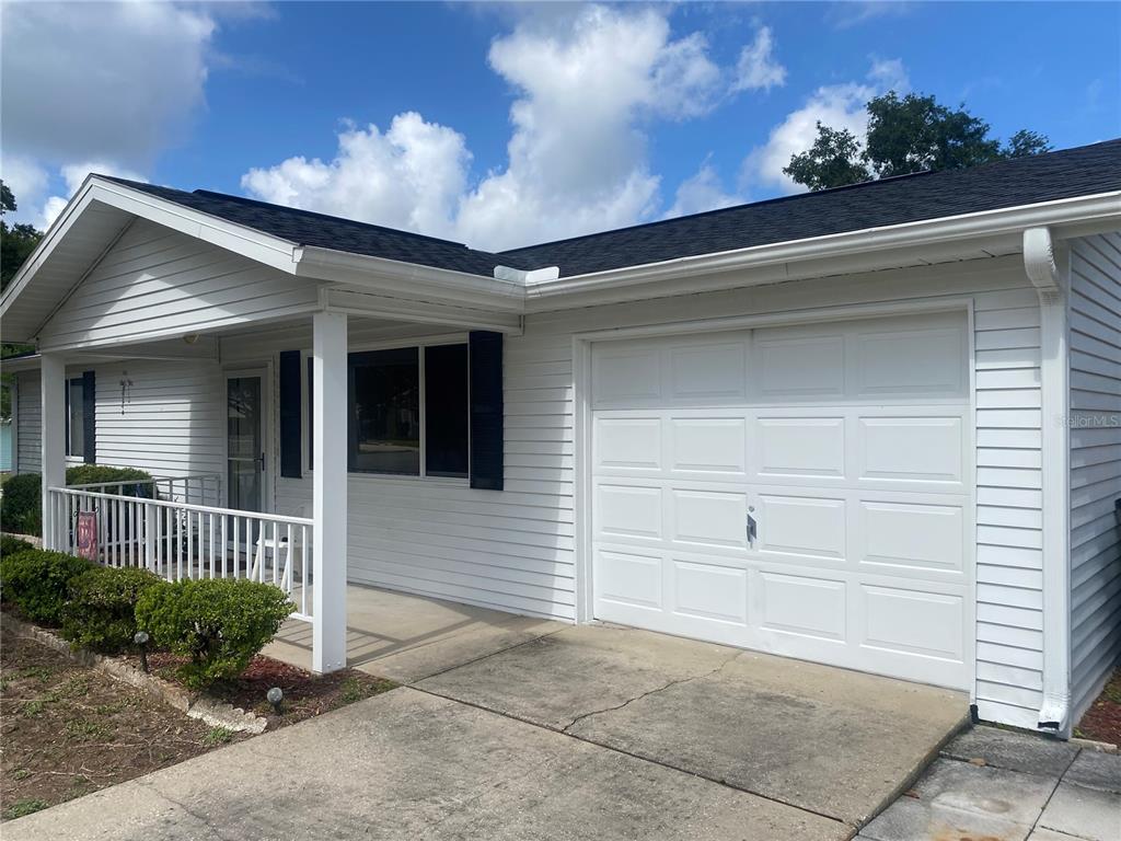 A white house exterior features a covered front porch, a garage, and a concrete driveway — 10986 SW 86TH TERRACE, OCALA, FL