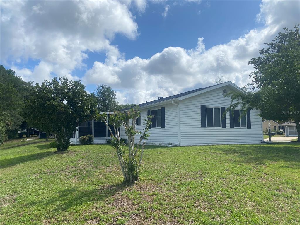 A white, single-story house with a screened-in porch sits on a grassy, tree-lined lot — 10986 SW 86TH TERRACE, OCALA, FL