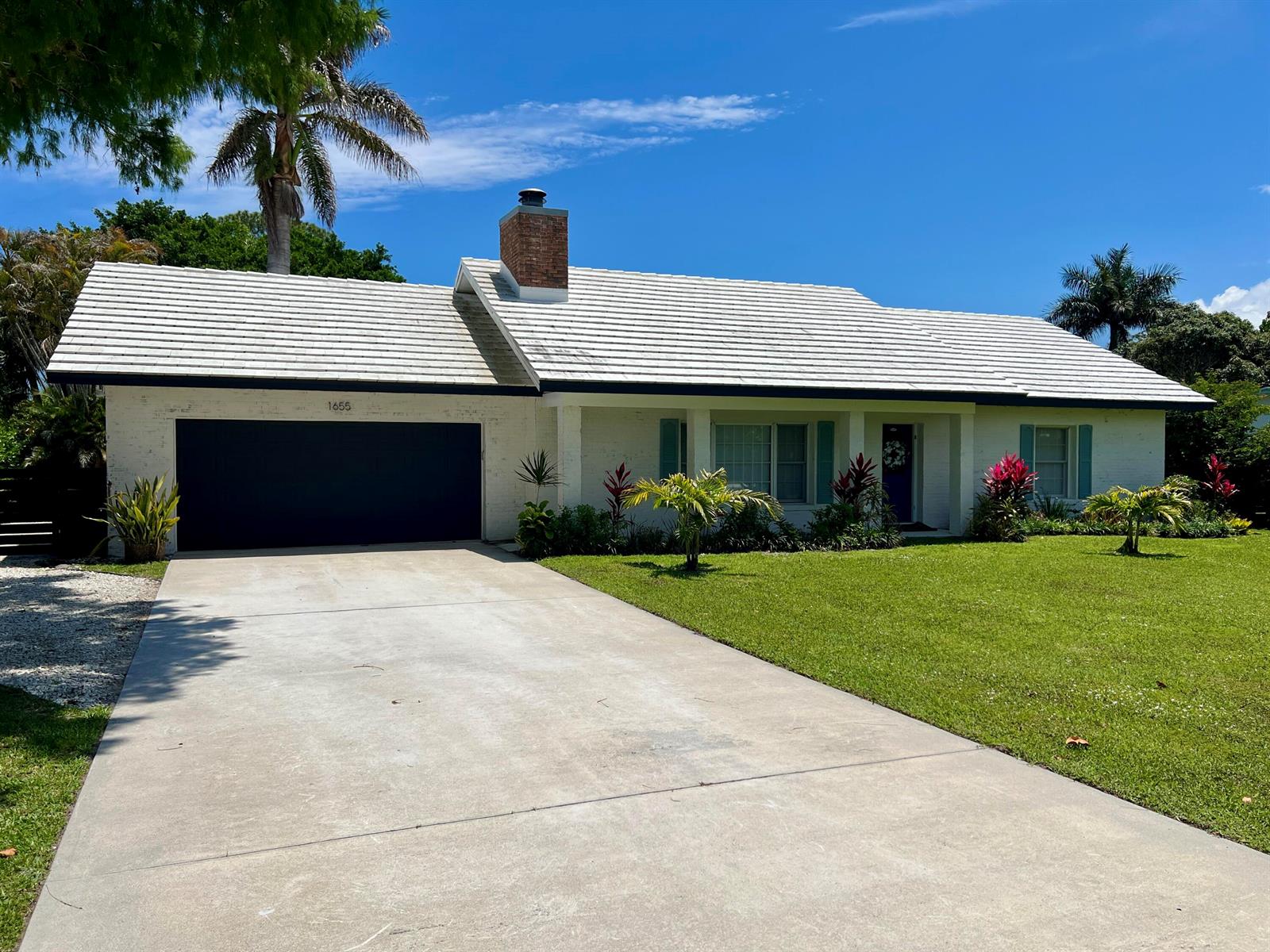 A single-story white brick house with a dark garage door and a tiled roof — 1655 NW Fork Road, Stuart FL 34994, STUART, FL