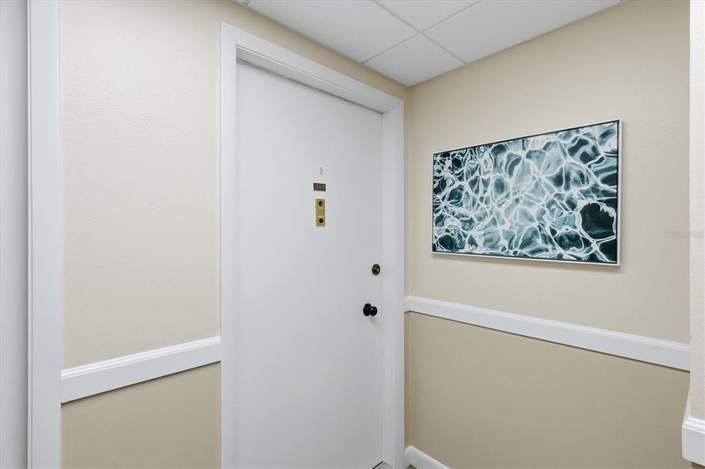 A white door with a peephole and locks sits beside a framed abstract wall art — 629 ALHAMBRA ROAD UNIT 702, VENICE, FL