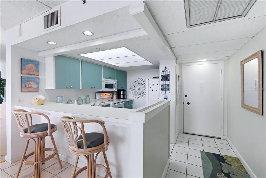 A kitchen with teal cabinets and a breakfast bar with two rattan stools — 629 ALHAMBRA ROAD UNIT 702, VENICE, FL