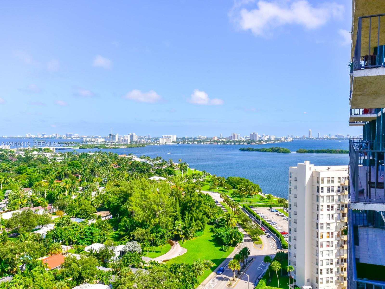 A tall, teal-accented residential high-rise building stands against a blue sky with scattered clouds — 780 NE 69th St # 1908, Miami FL 33138, MIAMI, FL