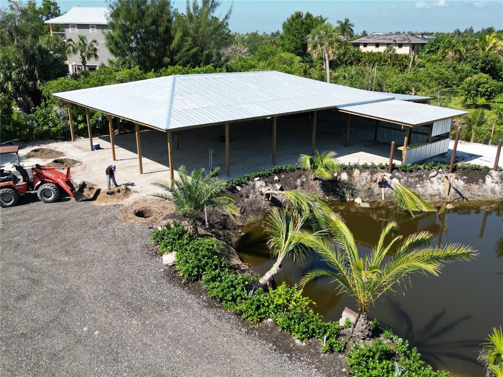 An aerial view shows a large metal-roofed pavilion next to a pond and construction equipment — 12242 EAGLES NEST DRIVE, BOKEELIA, FL