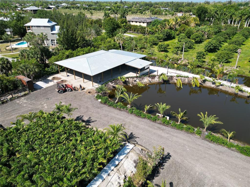 An aerial view shows a metal-roofed pavilion next to a pond and gravel driveway — 12242 EAGLES NEST DRIVE, BOKEELIA, FL